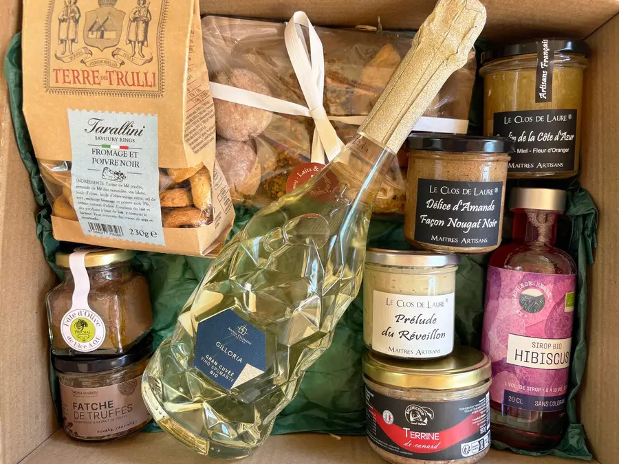 Un panier gourmand ouvert vu de dessus, sur papier de soie vert : pâte d'olive de Nice, fatche de truffe, prosecco, tarallini des Pouilles, douceurs des Abruzzes et tartinables niçois.